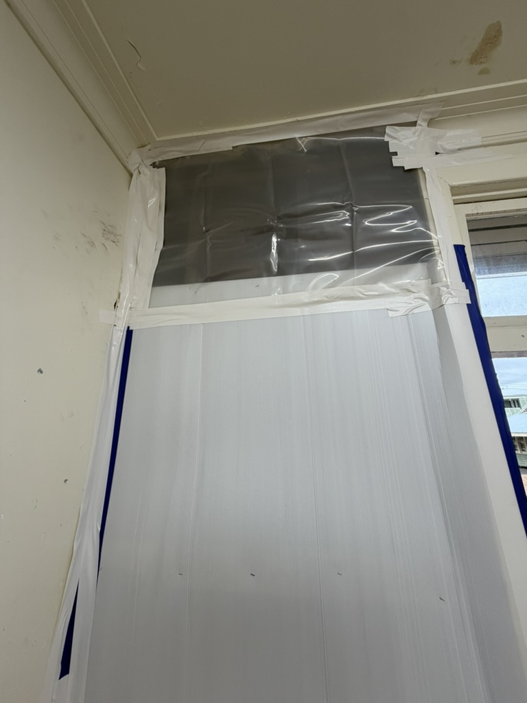 Interior opening sealed with plastic sheeting and tape, water-stained ceiling